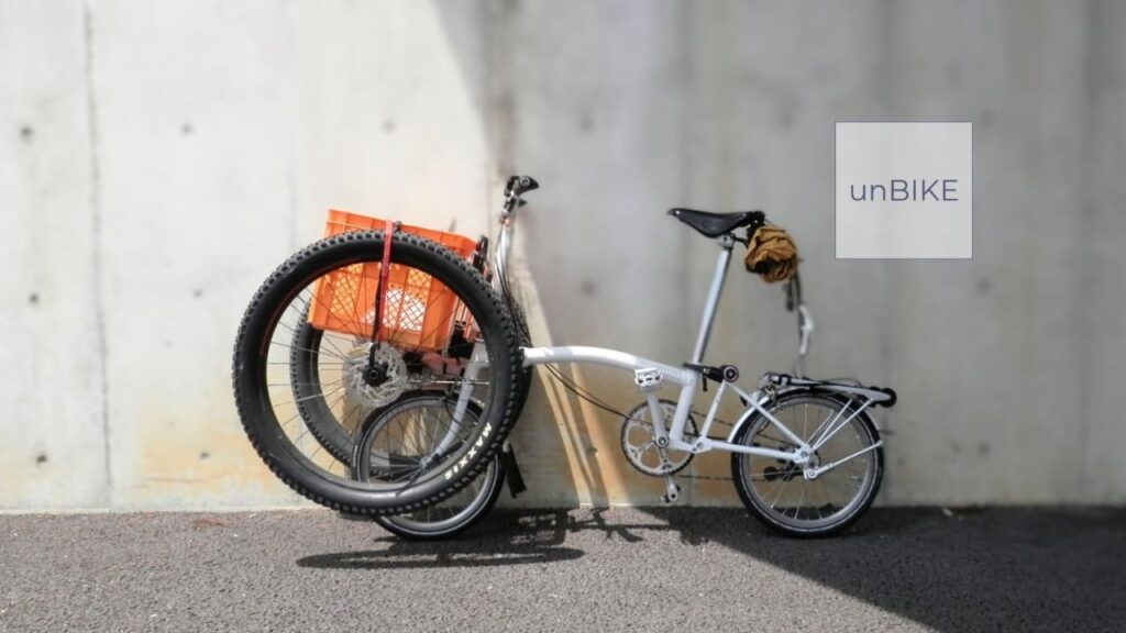 前カゴにマウンテンバイクのタイヤがくくりつけられた折りたたみ自転車のブロンプトン