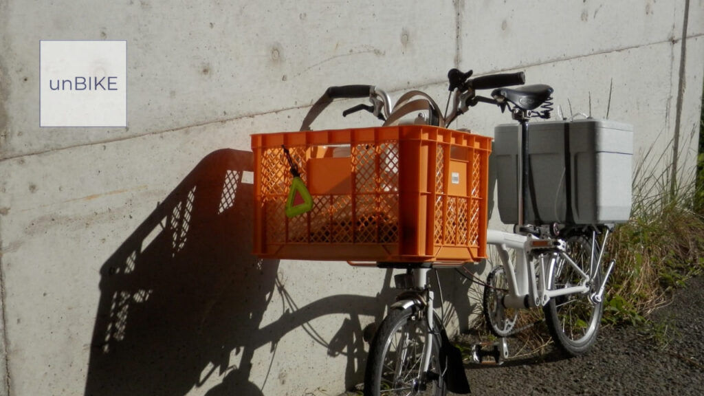 壁に立てかけられた折りたたみ自転車のBROMPTON。大きなオレンジ色の前カゴが付いている